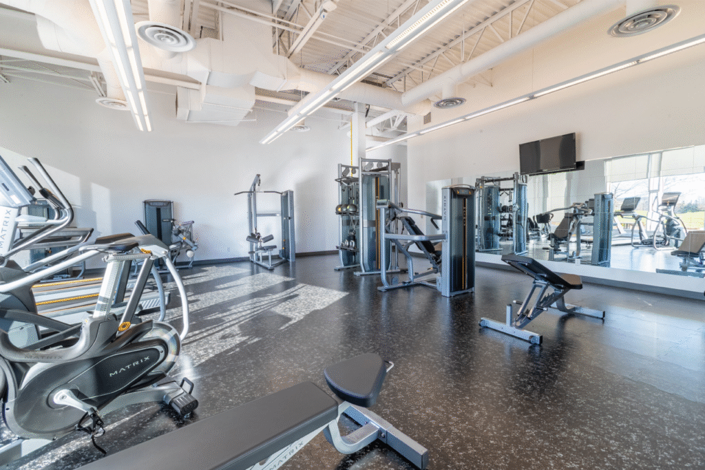 Fully equipped fitness centre at Cora GRID coworking space in Waterloo featuring cardio machines, strength training equipment, free weights, and bright natural light for a healthy work-life balance.
