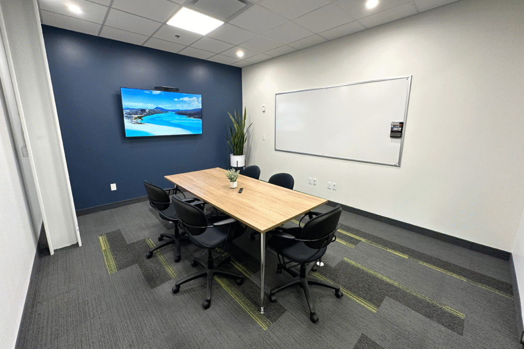 Modern meeting room at Cora GRID coworking space in Waterloo featuring video conferencing setup, wall-mounted display screen, whiteboard, ergonomic chairs, and collaborative workspace design.