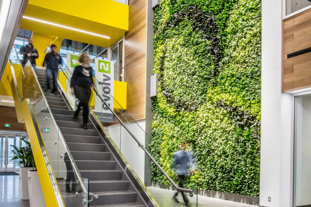 Lobby of evolv1 building in Waterloo featuring a striking green living wall, modern glass staircase with yellow accents, and sustainable interior design elements.